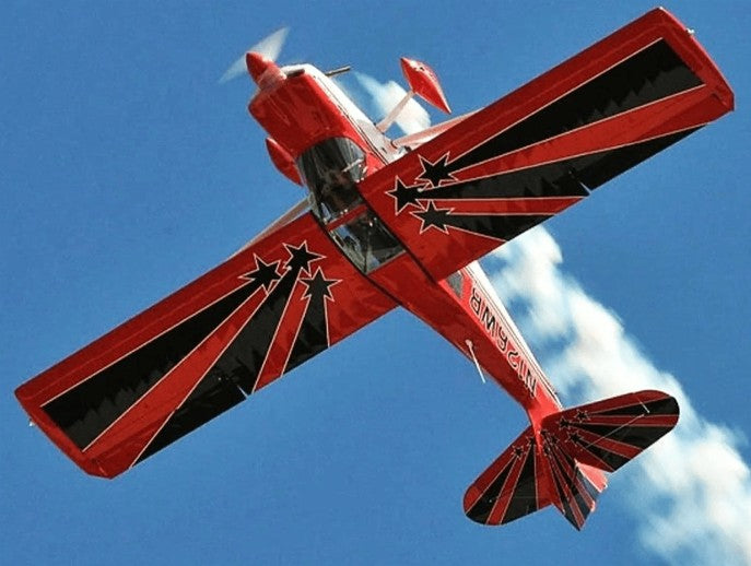 Red aerobatic airplane with black star design flying inverted against a blue sky