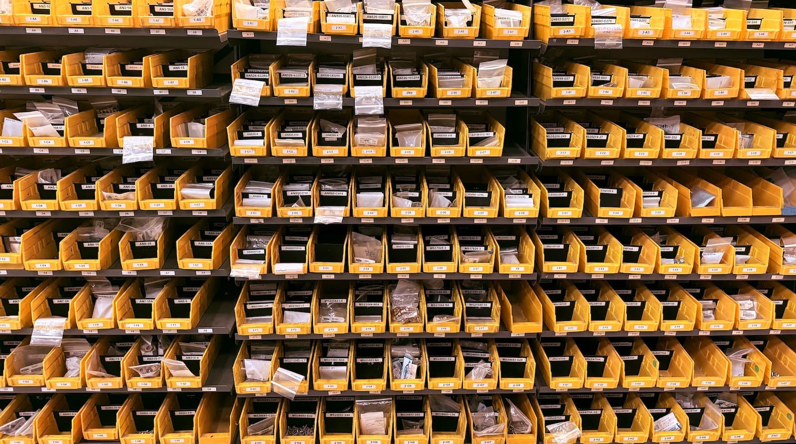 Shelving unit with yellow bins containing labeled items for aircraft maintenance. 