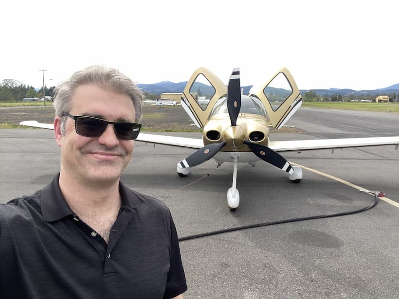 Man taking a selfie in front of a small airplane on a runway