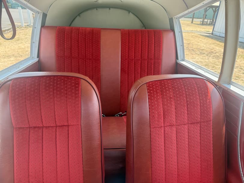 Red aircraft interior with two front bucket seats, a matching rear bench, and red-and-brown upholstered sides, photographed from inside the airplane.