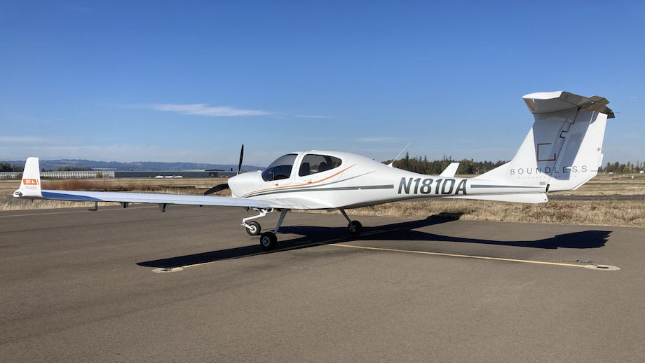 A white single-engine light aircraft parked on an airport tarmac under a clear blue sky.