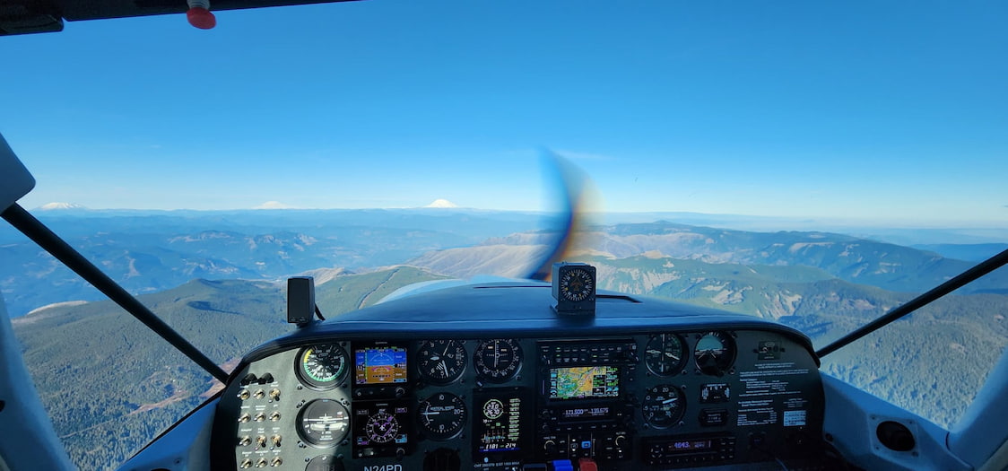 Airplane cockpit view with a clear blue sky and mountainous landscape