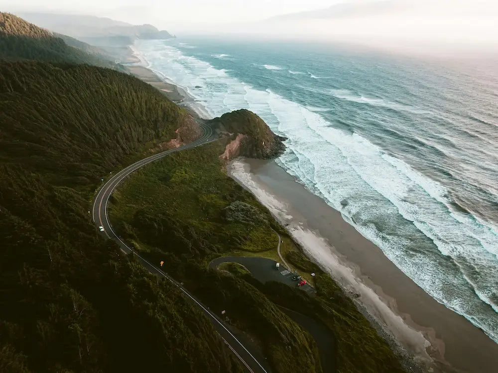 Winding road along the Oregon coast landscape with ocean waves and greenery.