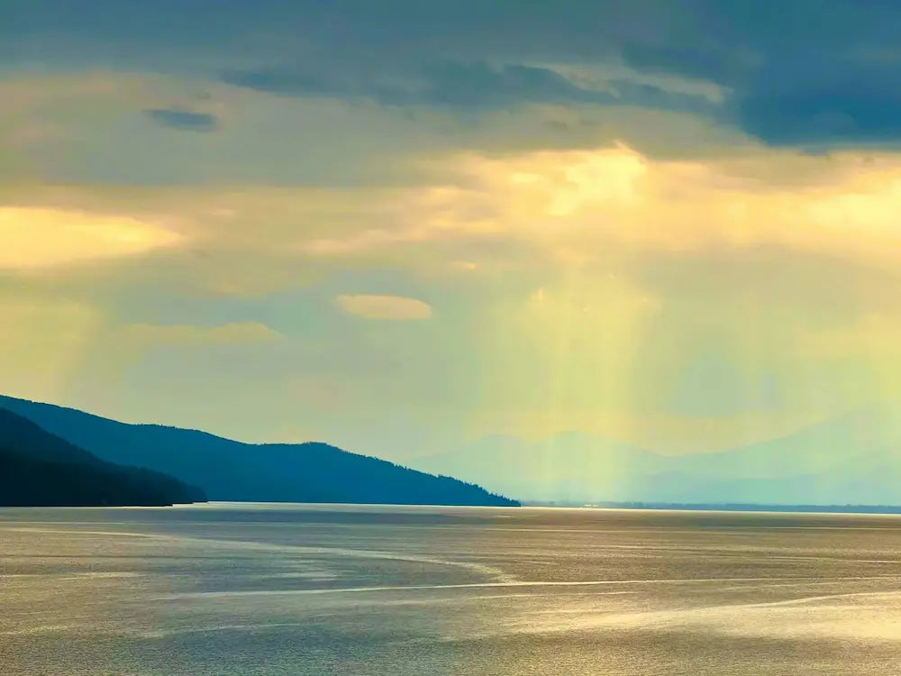Sunlight filtering through clouds over the lake at Sand Point with mountains in the background