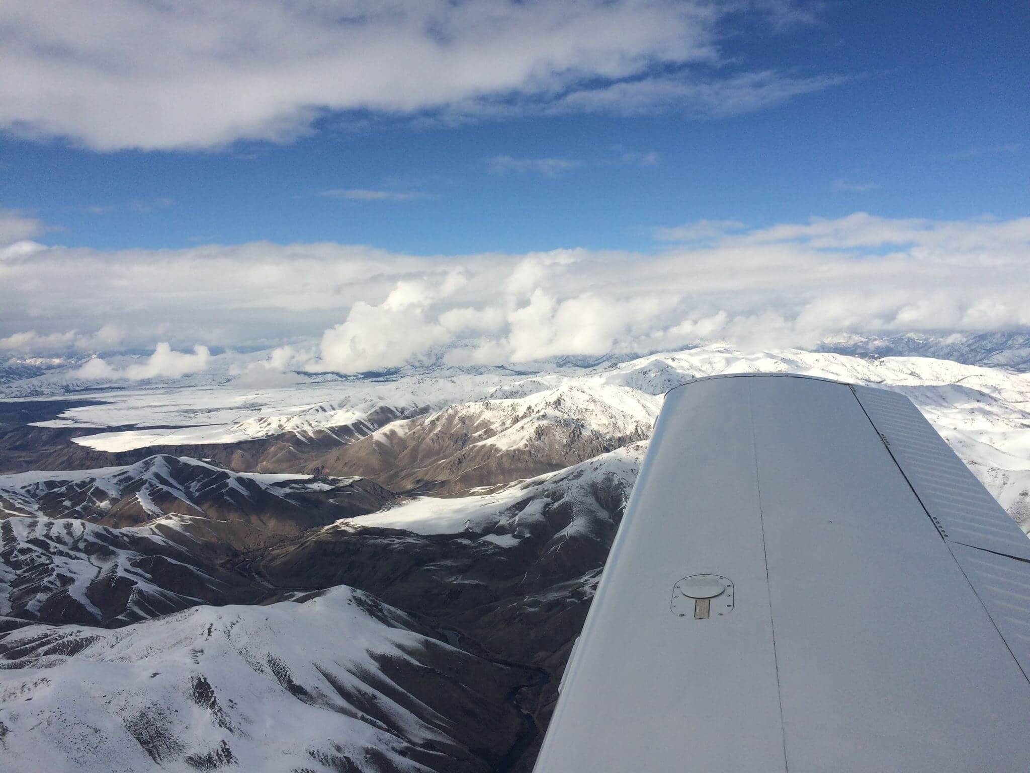 Aircraft wing over snow-covered mountains  of the Pacific Northwest with a blue sky and clouds.