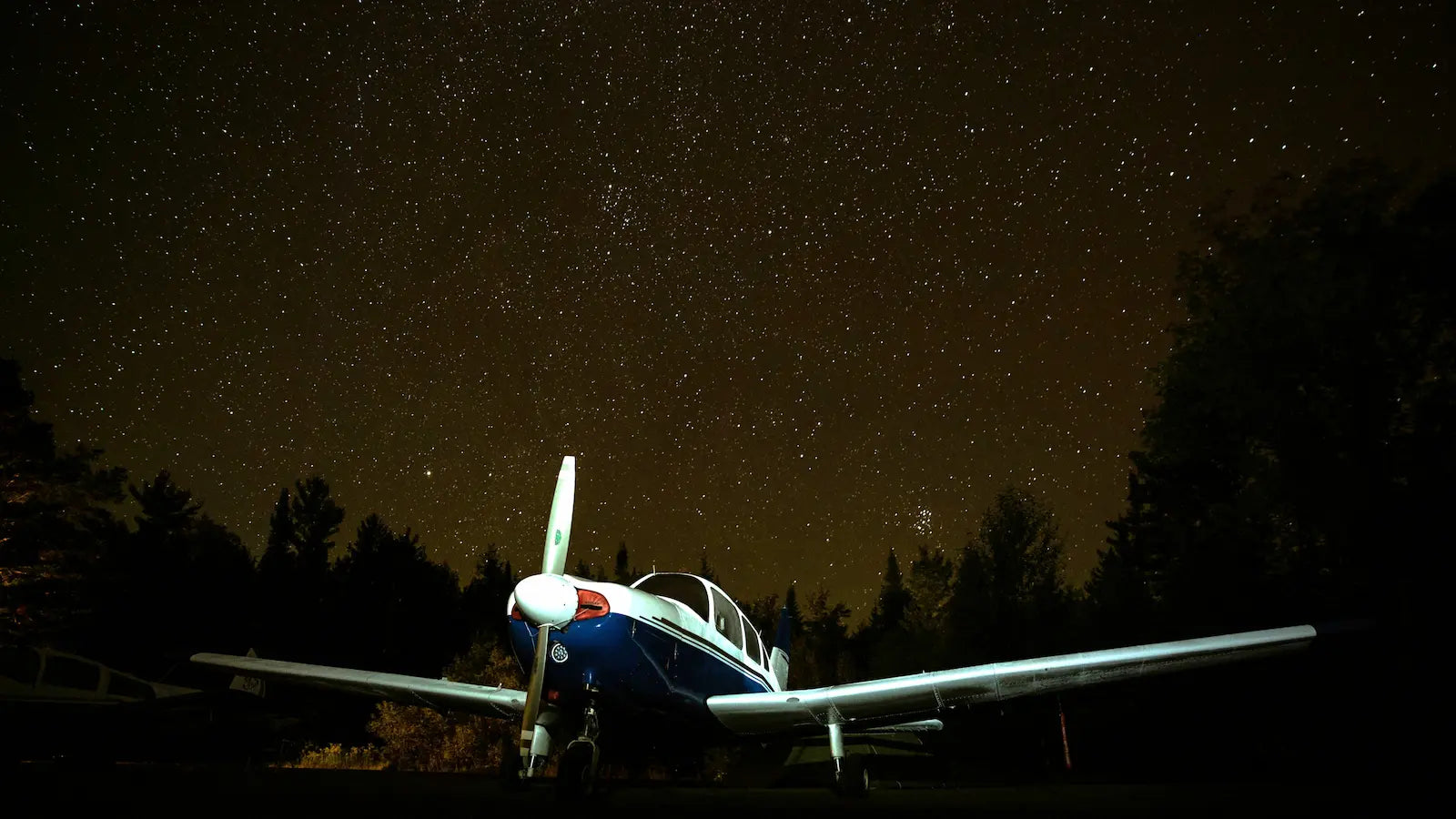 Small airplane under a starry night sky with trees in the background