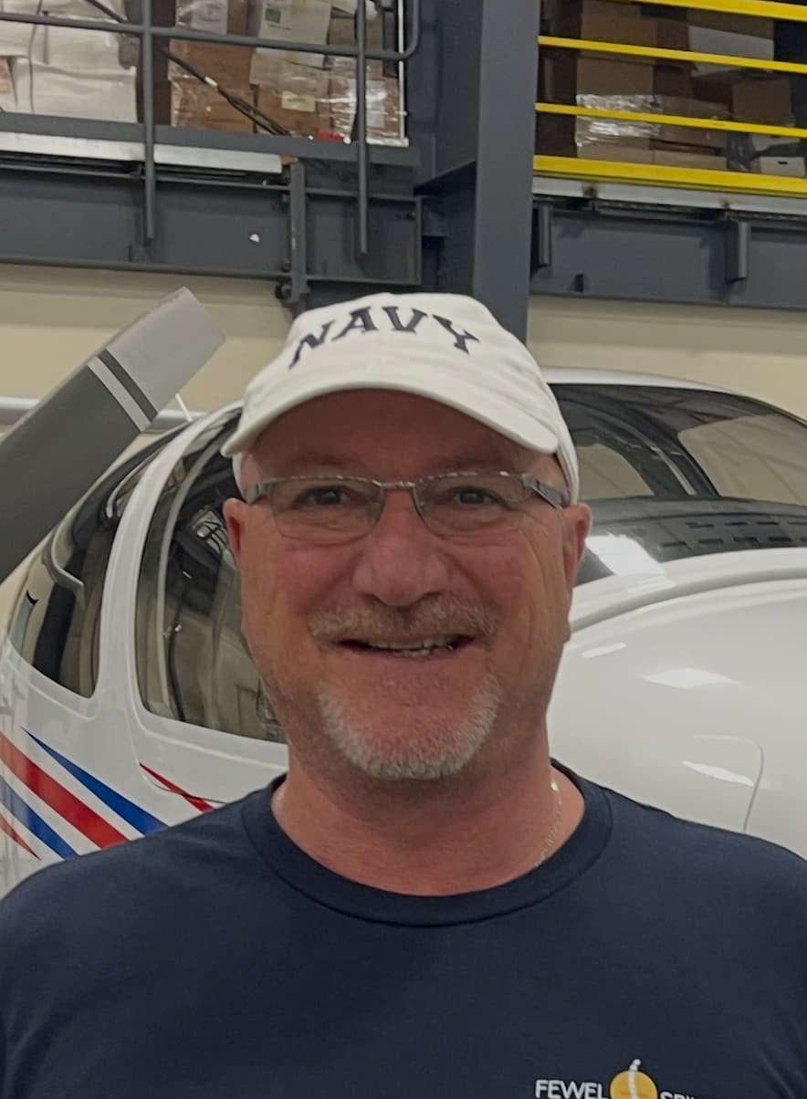 Man wearing a navy t-shirt with a logo standing in front of an airplane