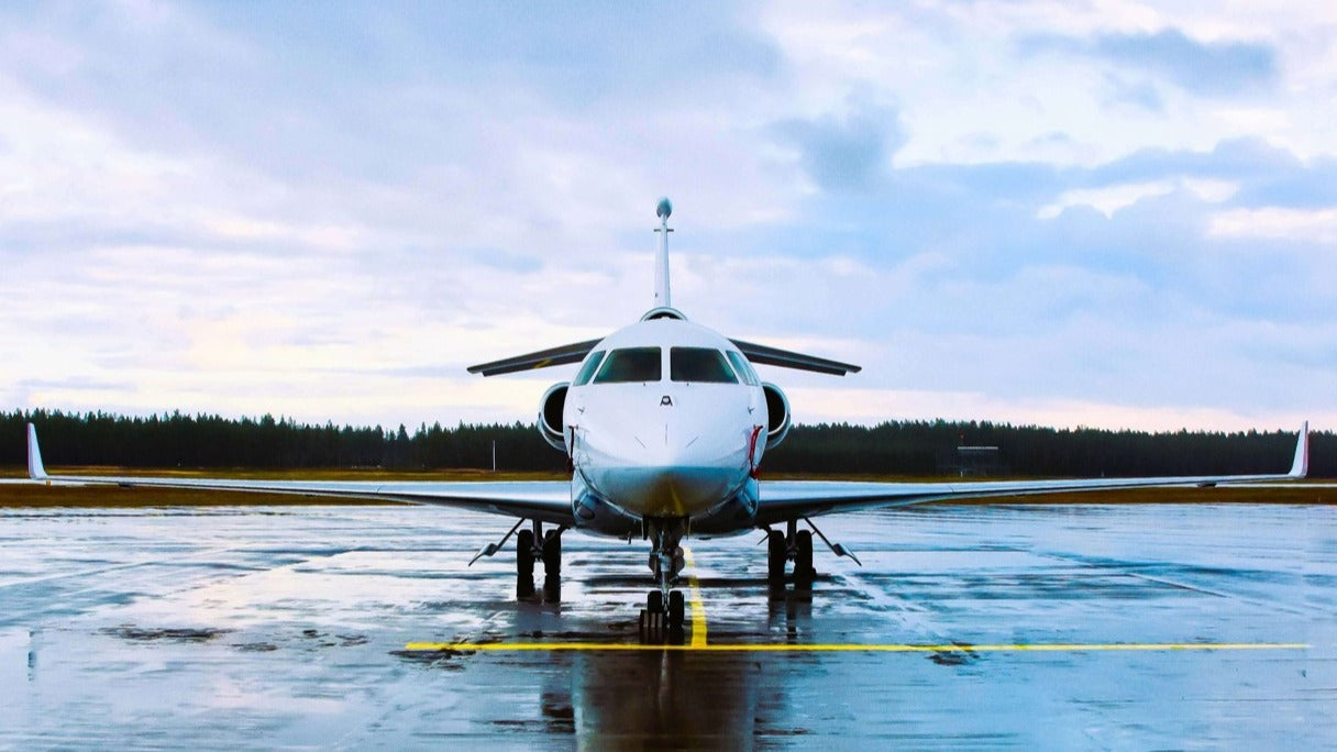 Jet airplane on a wet runway with a cloudy sky and pine trees in the background