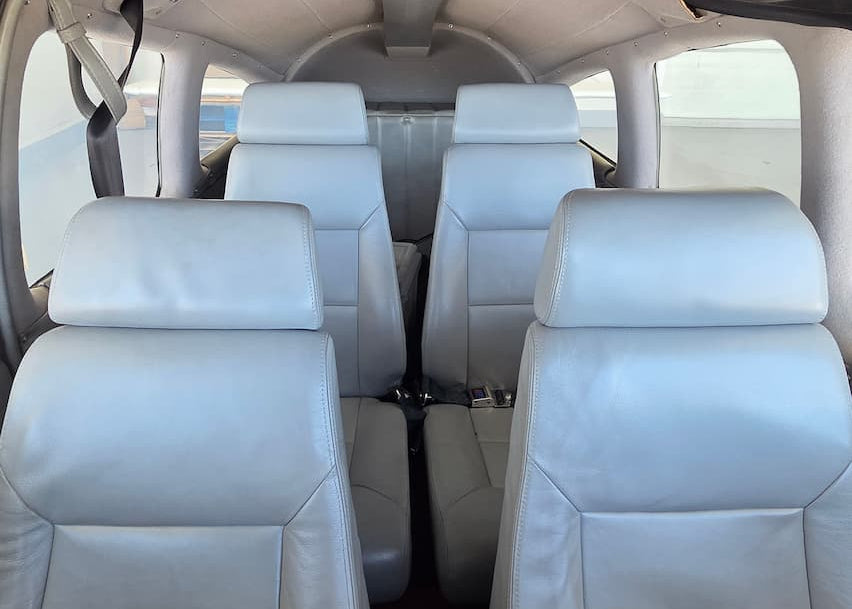 The interior of a small aircraft with four light gray leather seats arranged in two rows, viewed from the cockpit overhead.