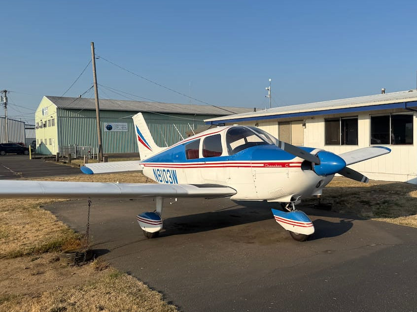 A small white, blue, and red single-propeller airplane parked on an asphalt lot tie-down.