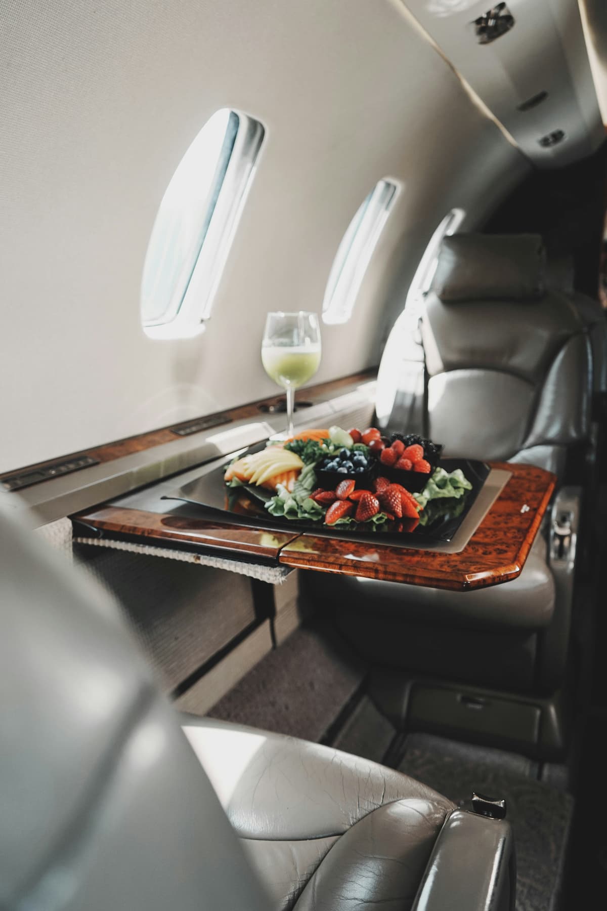 Luxurious airplane interior with a tray table set for a meal, featuring a glass of white wine and a plate of food for a private charter.