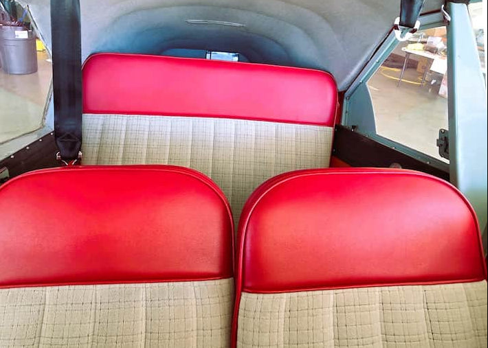 A pair of vintage aircraft seats with bright red vinyl headrests and beige textured bucket seats, viewed from the cockpit of the airplane.